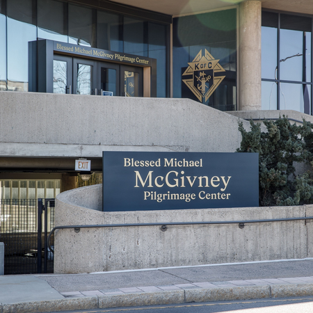 Black and gold Blessed Michael McGivney Pilgrimage Center signage on concrete exterior of building