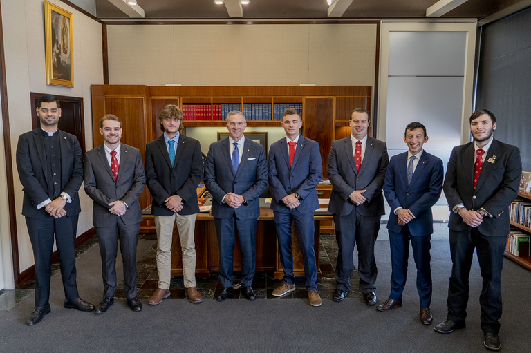 College knights pose for a photo in front of a Father McGivney statue