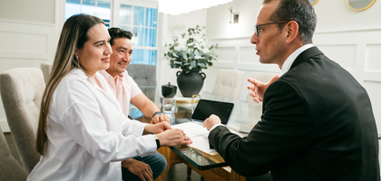 An agent sits and talks to a couple at a dinning room table.