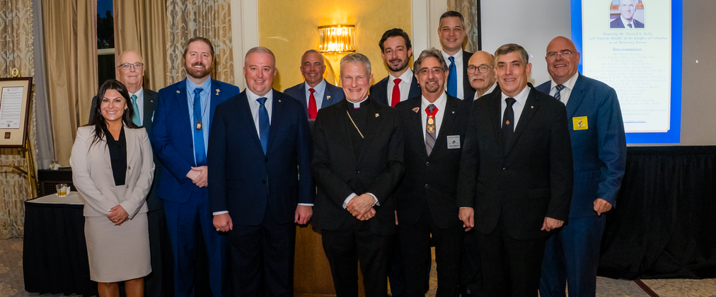 Archbishop Timothy Broglio of the Archdiocese for the Military Services, USA, is pictured with Supreme Director Jeffrey Crouch (fourth from left) and other representatives of the Knights and the Saint John XXIII Foundation in Charleston, S.C., on Oct 23. On behalf of the Order, Supreme Knight Patrick Kelly (pictured on screen at right) was recognized as honorary patron at the reception.
