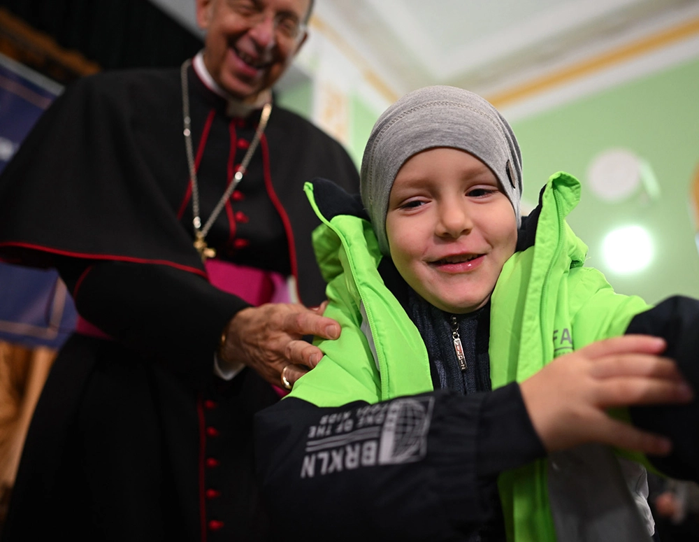 Archbishop Lori helps put a new coat on a child