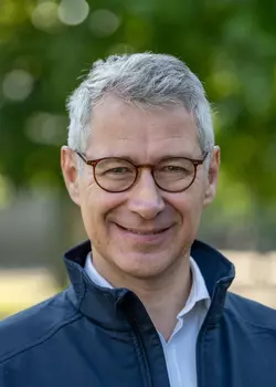 A portrait of Arnaud Bouthéon, wearing glasses and a blue jacket.