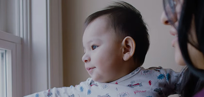 A mother holding her baby, who is looking out a window.
