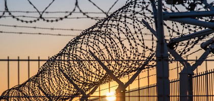 Barb wire on top of a tall fence.