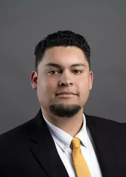 Headshot of Blake Nixon, who smiles while wearing a black suit and a gold tie