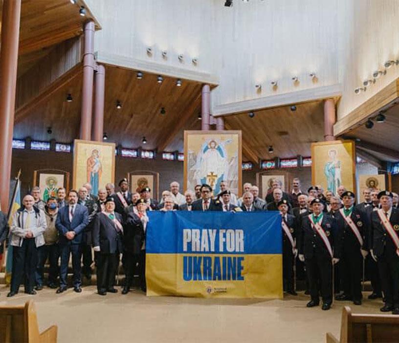 A group of people standing in a church, holding a large banner that reads 'Pray for Ukraine'. 