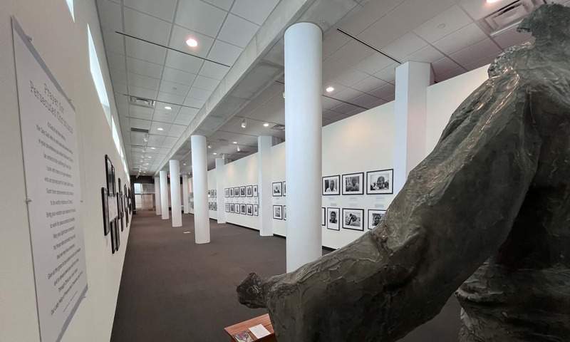 Overlooking the shoulder of a statue of Christ the Redeemer from a destroyed church in Nigeria, black and white photographs featuring persecuted Christians line the walls at the Shrine.