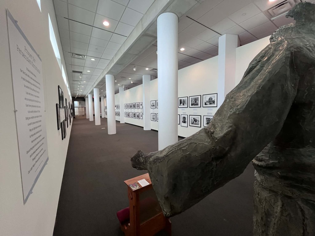 Overlooking the shoulder of a statue of Christ the Redeemer from a destroyed church in Nigeria, black and white photographs featuring persecuted Christians line the walls at the Shrine.