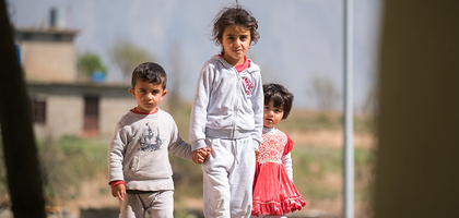 Christian refugee children hold hand while looking at the camera.