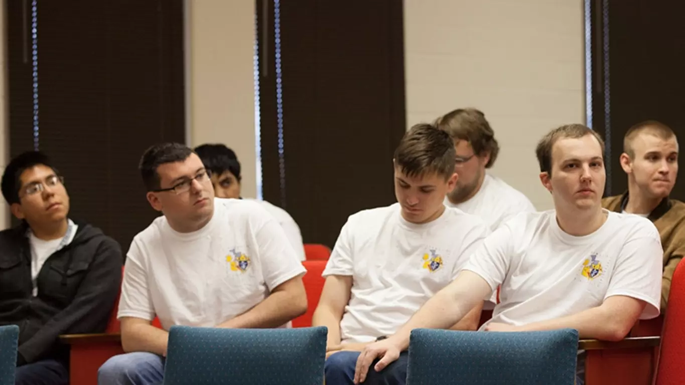 Three college Knights sit together in a lecture hall at their university.