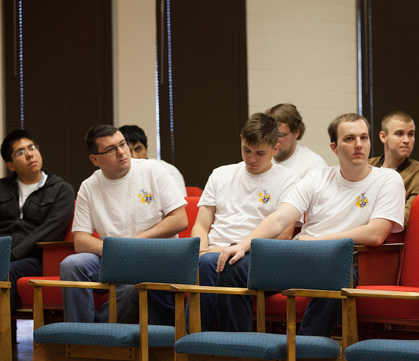 Three college Knights sit together in a lecture hall at their university.