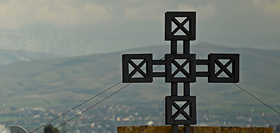 A cross on the summit of a mountain facing a valley