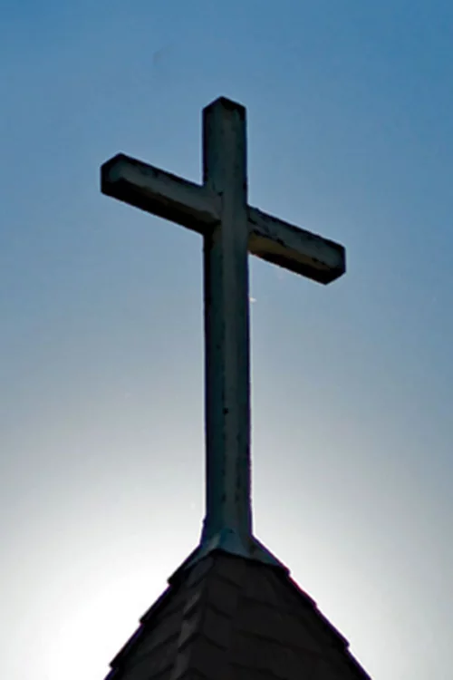 the sun and a clear blue sky behind a steeple cross