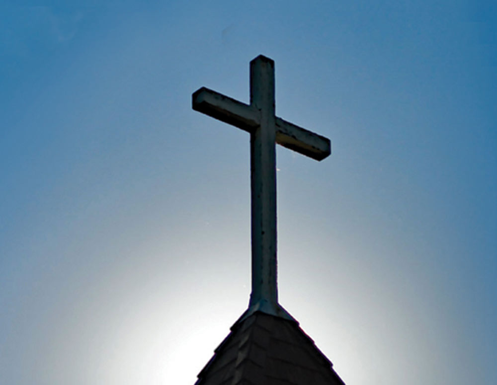 the sun and a clear blue sky behind a steeple cross