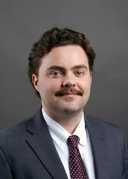 Headshot of David Spangler, who smiles while wearing a grey suit and a red tie
