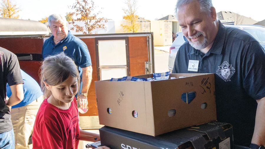 A Knight and child help pack supplies at a food distribution site.