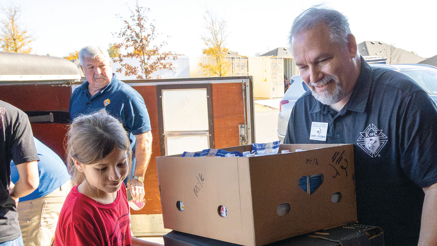 A Knight and child help pack supplies at a food distribution site.