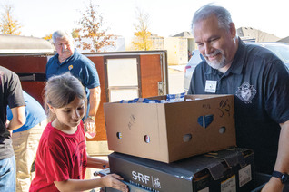 A Knight and child help pack supplies at a food distribution site.