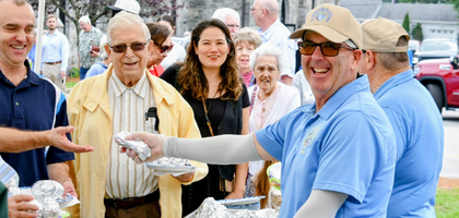 Massachusetts Past State Deputy Michael Lesperance wearing a blue Knights of Columbus polo shirt poses for a smile as he serves food to adult attendees.
