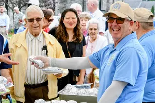 Massachusetts Past State Deputy Michael Lesperance wearing a blue Knights of Columbus polo shirt poses for a smile as he serves food to adult attendees.