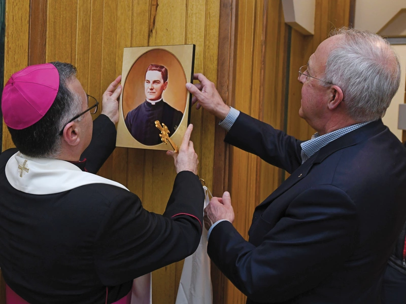 Then-Supreme Knight Carl Anderson and Archbishop Warda place an image of Father Michael McGivney in McGivney House.