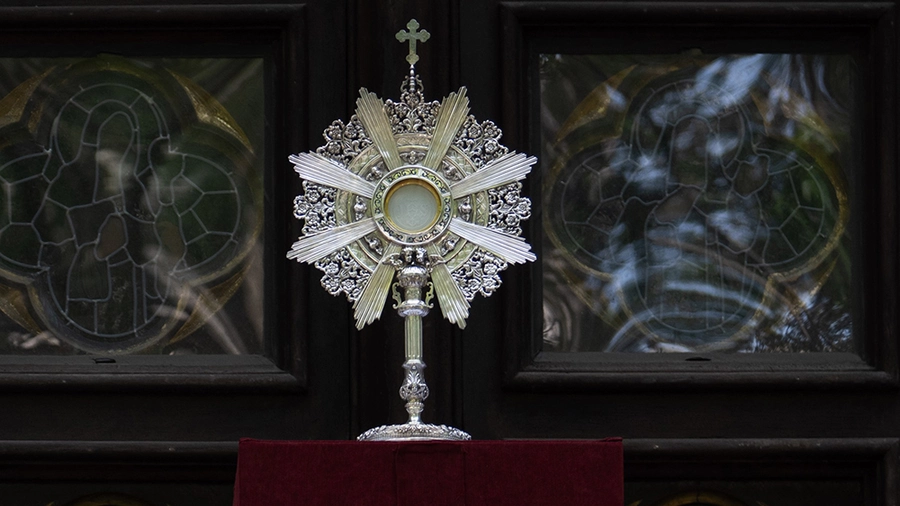 The Eucharist in a monstrance in front of stained glass windows.