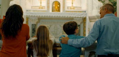 Man kneeling with family praying at alter.