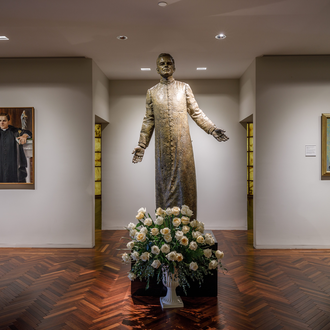 Statue of Father Michael J. McGivney in the McGivney Gallery at the Blessed Michael McGivney Pilgrimage Center, with portraits of him on either side.