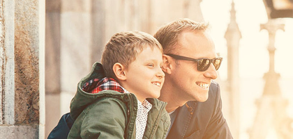 A father and his young son look at their surroundings from an outdoor balcony.