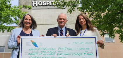 Grand Knight Lou Curti dressed in a grey suit presents a large $1,000 paper check.  He poses for a photo with two women both wearing business casual attire.