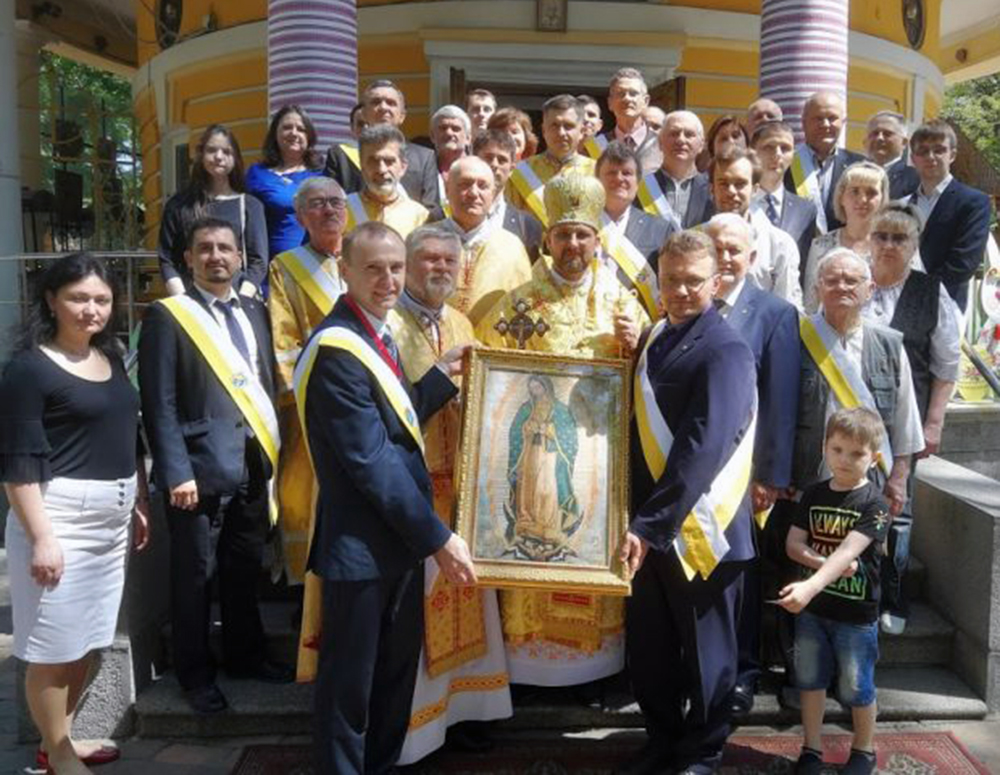 Group of Ukrainian Knights, priests, and their families stand with an image of Our Lady of Guadalupe after blessing the image.