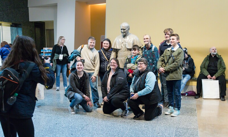 A group of pilgrims pose with a statue of Saint John Paul II on the lower level of the Shrine