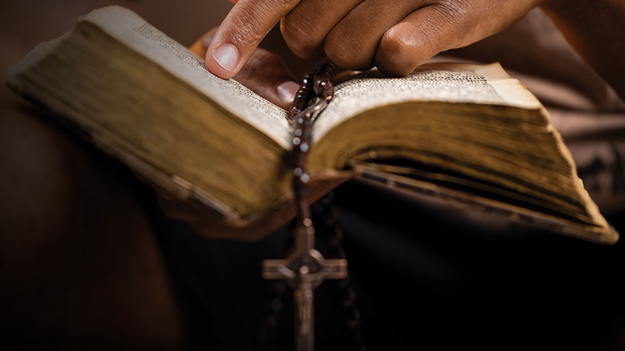 Person holds a bible with a rosary draped across the pages.