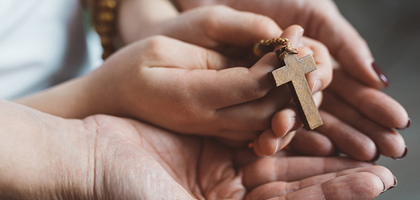 A mother and child's hands together while holding a rosary.