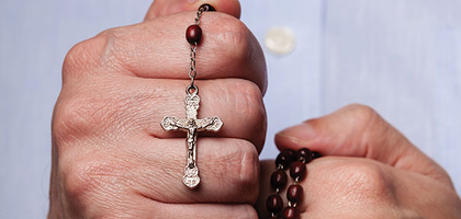 Male hands holding a rust red colored rosary