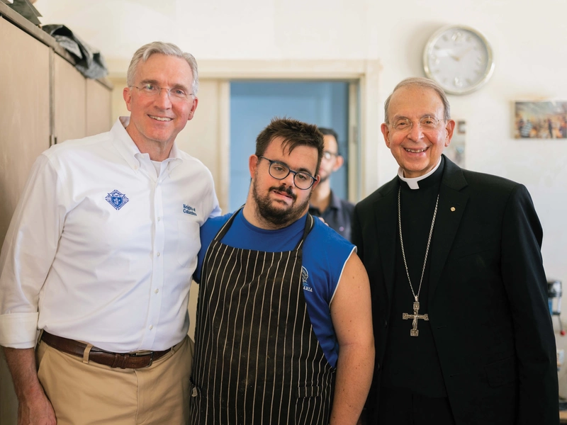 The supreme knight and supreme chaplain stand with a worker at the Piccirillo Handicraft Center in Bethlehem.