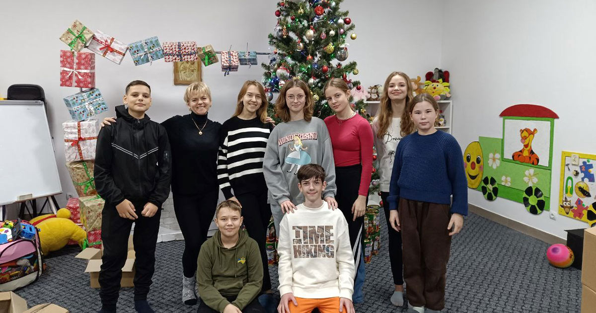 Teenagers kneeling and standing in front of a Christmas tree