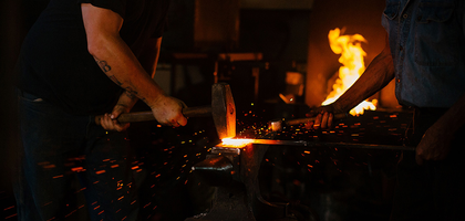 Hammer coming down on hot metal over anvil with sparks flying.