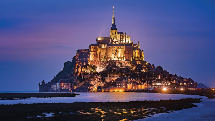 The renowned Mont-Saint-Michel Abbey is seen illuminated at dusk.