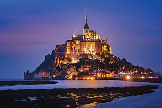 The renowned Mont-Saint-Michel Abbey is seen illuminated at dusk.