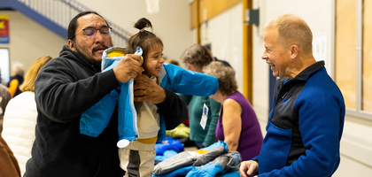 Shane Hanson (right), a member of Msgr. Robert A. Feehan Council 1604 in Bismarck, N.D., shares a smile with a young girl as her dad helps her try on a new winter jacket at a Coats for Kids distribution at St. Mary’s Elementary School. 