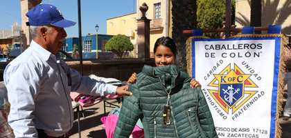 Deputy Grand Knight Rodrigo Sandoval of San Francisco de Asís Council 17128 in Nochistlán, Mexico West, gives a new coat to a girl at San Pedro Apóstol Parish in Apulco.