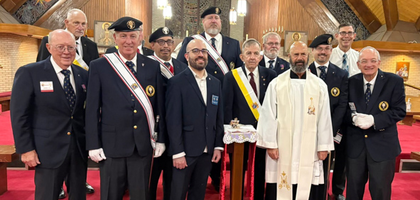 Several Knights stand together inside of a church dressed in formal attire in front of a silver rose resting on a podium.