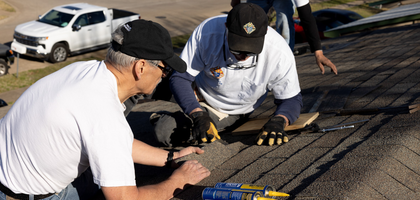 Men on a roof with roofing materials replacing shingles in order to repair damage to the roof.