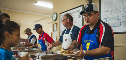 Knights serving food for those who are in need. A man adds rice the plate of a young girl.