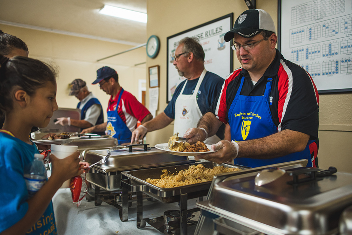 Knights wearing Knights of Columbus aprons serve food to children.
