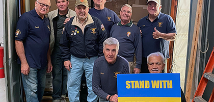 Knights of Columbus across the U.S. are delivering tons of humanitarian aid to Ukraine and supporting refugees and orphans through direct action and local initiatives. A group of men stand in the back of a delivery truck and pose for a group photo. One man holds a sign that says, "Stand with Ukraine."
