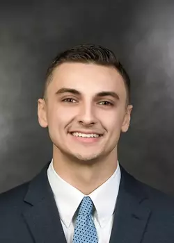 Headshot of Levi Edelman, who smiles while wearing a black suit and blue tie.