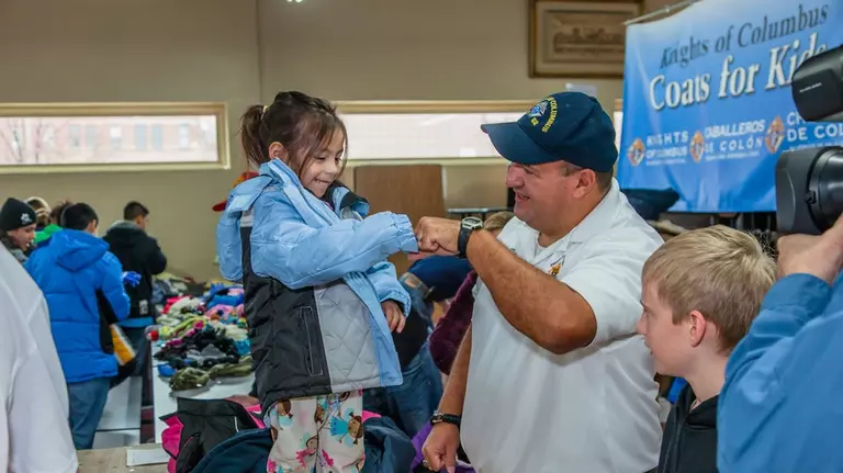 A Knight and young girl fist bump in celebration at a Knights of Columbus Coats for Kids event