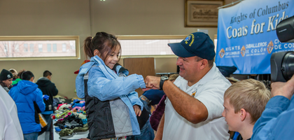 A Knight and young girl fist bump in celebration at a Knights of Columbus Coats for Kids event